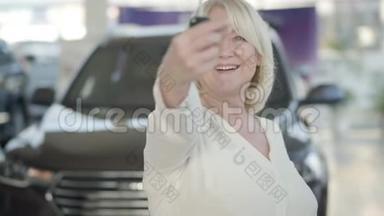特写成熟的白种人幸福的女人在展厅炫耀汽车钥匙。 兴奋的金发女郎在镜头前展示钥匙